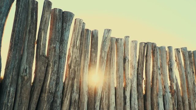 holzzaun aus gro&szlig;en baumst&auml;mmen, im hintergrund sonnenuntergang mit sunflare
