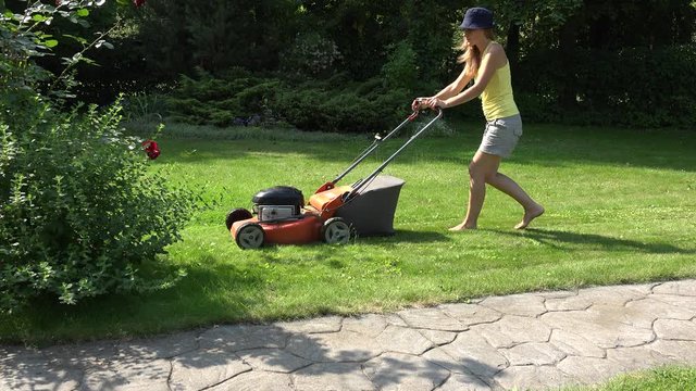 Young girl mowing green grass lawn with orange push mower. 4K