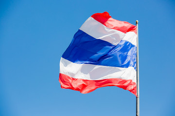 waving Thai flag of Thailand with blue sky background.
