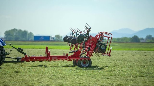 We can see a tractor and an agricultural machinery and they are driving on the lawn. Certain parts of the rotary hay rakes are folding up.
