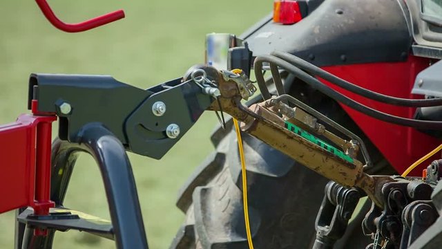 A trailer connector is moving up and then down again. A rotary hay rake is connected to the tractor because a farmer is preparing hay.
