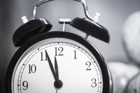 black and white image of alarm clock showing almost twelve o'clock. extreme closeup. selective focus