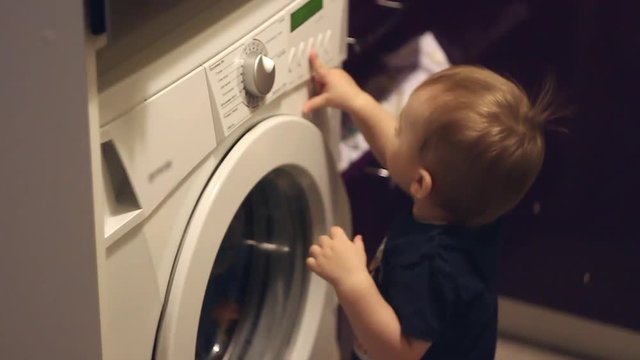 Baby boy pushes the button on wahing machine.