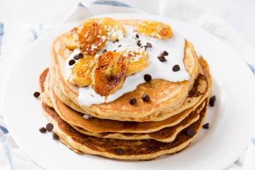 Banana pancakes with yogurt and chocolate chips on white plate, close up view