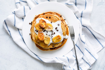 Pancakes with caramelized bananas, natural yogurt, chocolate chips and coconut shavings on white...