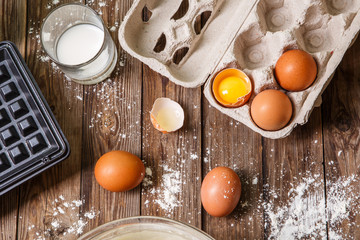 Making waffles at home - waffle iron, batter in bowl and ingredients - milk, eggs and flour.