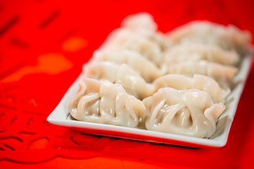 Chinese dumplings and paper-cut on red background. People will eat dumplings during Chinese New Year to pray for good fortune.