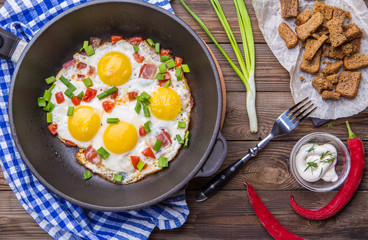 Fred eggs in pan with tomatoes and green fresh onion.