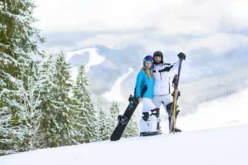 Happy couple standing on a mountain top. Couple skiing and snowboarding outside in the mountains.