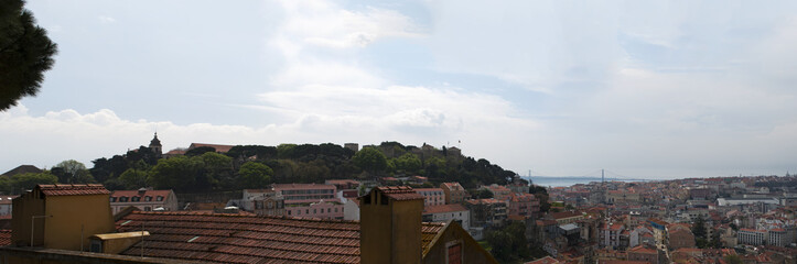Fototapeta na wymiar Lisbona, 01/04/2012: skyline di Lisbona con vista sui tetti rossi, i palazzi della Città Vecchia e il Castello di San Giorgio, le cui mura e le torri furono costruite durante l'occupazione moresca