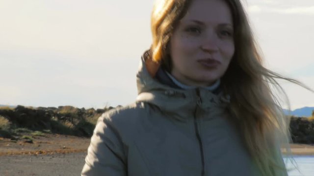 medium shot of young tourist is walking on black volcanic beach in Reykjavik, smiling blond woman