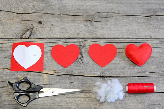 How to make stuffed felt heart for Valentine's day. Handmade red felt heart, cut felt pieces, paper template, scissors, thread on a wooden background. Simple and cheap Valentine's day crafts