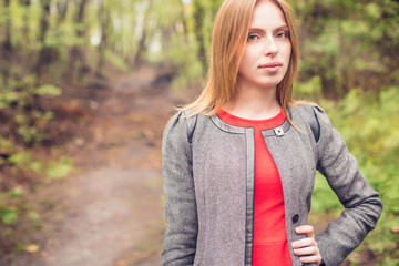 Cute girl on the background of the forest, where the path leads into the distance on the perspective. Young smiling woman holding a hand in his belt and looks at the camera.