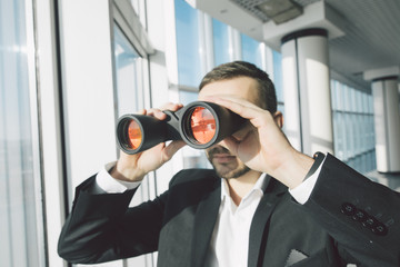 Business man looking with binoculars over panoramic windows