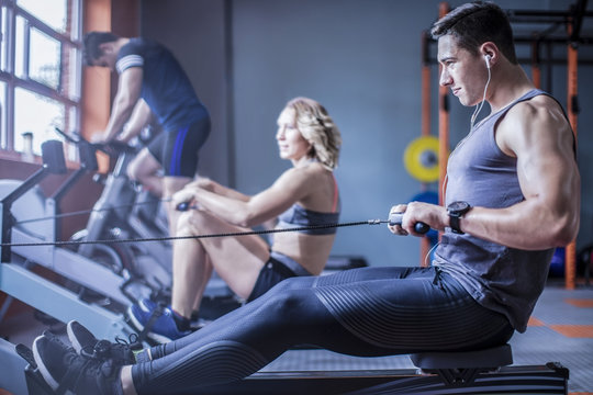 Young man exercising on rowing machine in gym