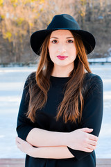 Winter portrait of a happy beautiful girl with brown hair in winter forest on the lake. Woman wearing a hat and bright clothes. Winter atmosphere, nature and freedom concept. 