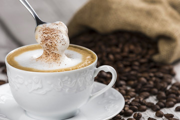 Cup of Cappuccino with Spoon and foam / Composition of Cup of Cappuccino and spoon with foam, sack of coffee beans on white wooden table