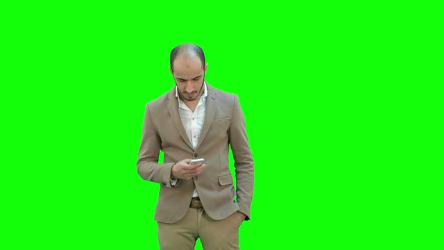 Business man walks in texting on the phone on a Green Screen, Chroma Key.