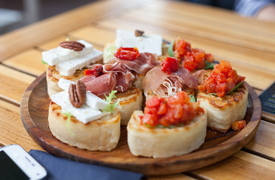 Fresh Toasted Slices Bread with Tomatoes, Ham and Brie Cheese on wooden plate, shallow focus