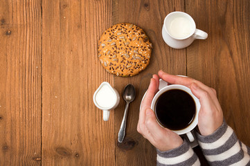 Cup of coffee in woman hands, cookie on old wooden table.