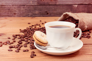 Cup of coffee, saucer with cookies, roasted coffee beans in sack
