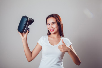 Attractive and happy woman holds virtual reality goggles on grey background. VR headset.