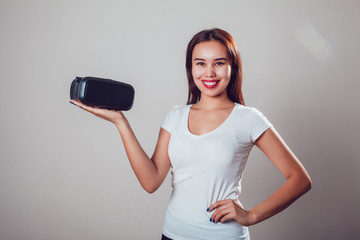 Attractive woman holds virtual reality goggles on grey background. VR headset.