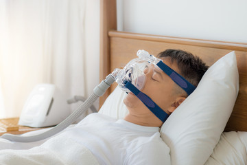 Obstructive sleep apnea therapy, Man wearing CPAP mask.
CPAP:Continuos positive airway pressure  therapy.Happy and healthy senior man breathing more easily during sleep  on his back without snoring. - obrazy, fototapety, plakaty