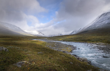 Autumn landscape in clouds and sunlight lighting up part and snow covered mountains