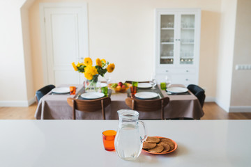 Coziness at home. Modern interior design. Decanter with water and plate with waffles in the kitchen, bouquet of sunflowers on the dining table on the background.