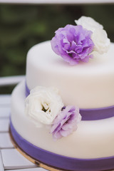 Fototapeta na wymiar White wedding cake with purple flowers decoration outdoors on wooden modern chair.