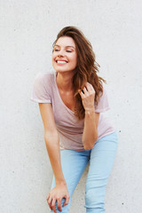 happy young woman standing against white wall and looking away