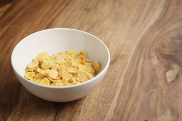 dry corn flakes in white bowl on wood table, copy space on right side