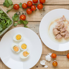 Tuna fish, boiled eggs, cherry tomatoes and baby spinach leaves on wooden background