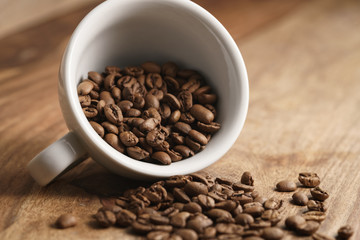 Fototapeta premium overturned cappuccino cup with roasted coffee beans on wood table, closeup photo