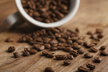overturned cappuccino cup with roasted coffee beans on wood table, closeup photo
