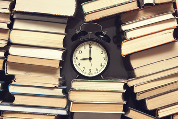 alarm clock showing nine o'clock among stack of old books background, selective focus, filter applied