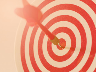 Red bullseye dart arrow hitting target center of dartboard. Concept of success, target, goal, achievement. Vintage with flare tone (selective focus)