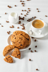 Oatmeal cookies, coffee grains and cup of hot coffee on white table