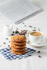 Oatmeal cookies, coffee grains and cup of hot coffee on white table