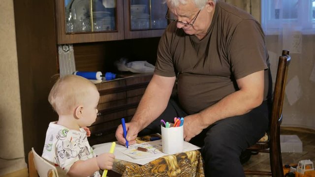 Grandfather with his grandson kid draws markers on paper. The boy looks carefully and help. Smiling and surprised. The concept of teaching children at home