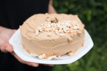 woman holding homemade coffee cream cake on white plate, partly top with slice cashew nut