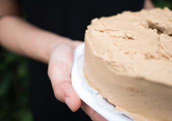 woman holding homemade coffee cream cake on white plate
