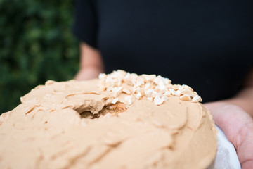 woman holding homemade coffee cream cake on white plate, partly top with slice cashew nut