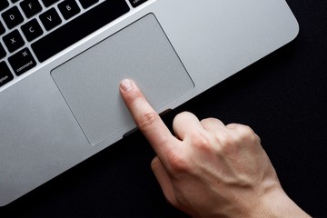 Hand using trackpad on laptop over black background - obrazy, fototapety, plakaty