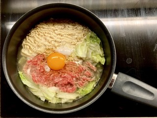 Cooking and boiling  instant noodle with chopping meat, vegetable and egg inside a pot which is heated by black stove 