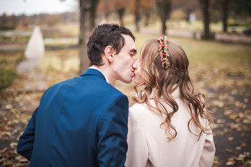 Newlyweds sit on the wooden bench in an autumn garden, back view