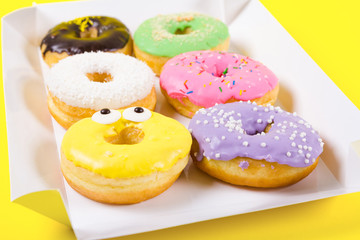 Strawberry, chocklate and other donuts in paper box on yellow background