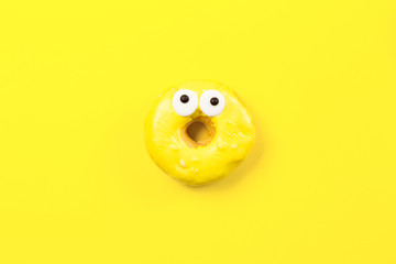 Round donut with eyes on yellow background. Flat lay, top view.