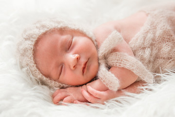 Новорожденный малыш в вязанном чепчике и боди спит на...